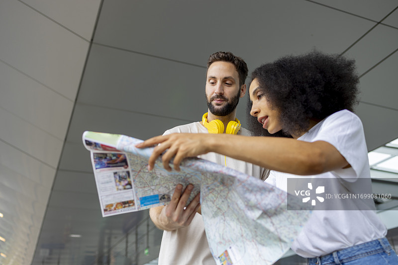 年轻白人男子和非洲裔女子在火车站等候，手持地图图片素材