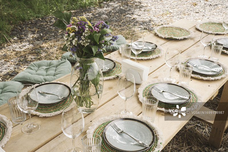 户外节日晚餐时尚餐桌布置，大木桌、陶瓷盘、酒杯和花瓶图片素材