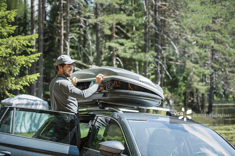 男子在车顶行李架上装载露营度假的货物箱图片素材