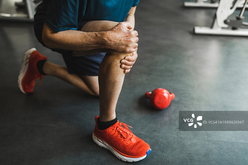 男人在健身房用壶铃锻炼时膝盖受伤，背景有复制空间，看不清人图片素材