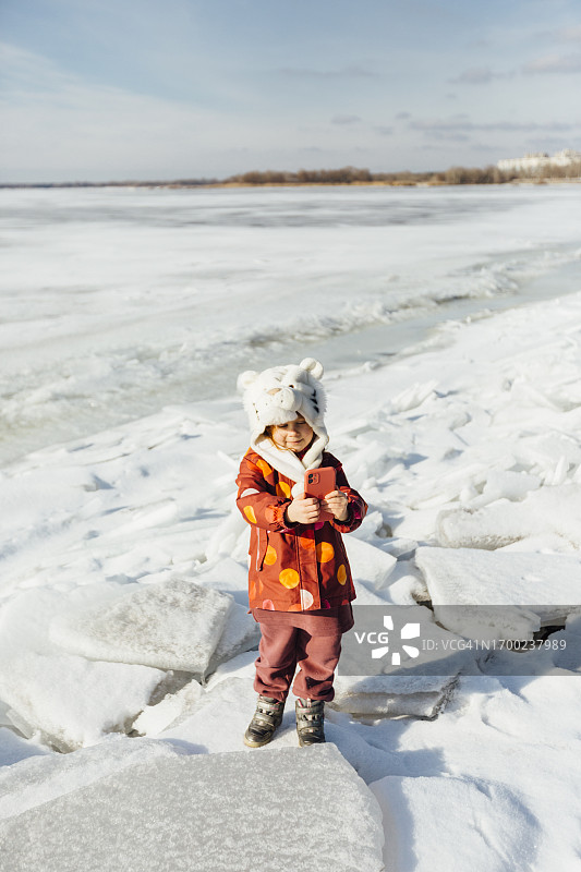 年轻女孩用手机拍摄结冰的滨水区图片素材