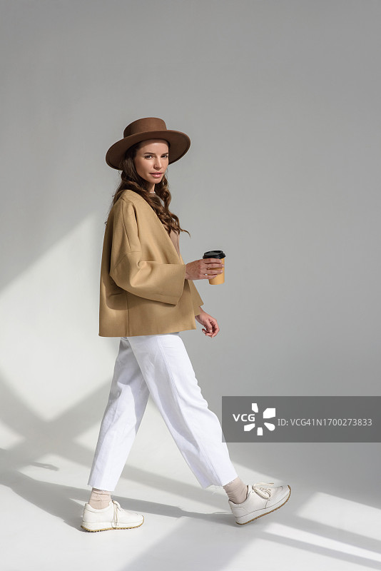 穿着品牌服装，手拿咖啡杯的时尚模特在影棚摆姿势图片素材