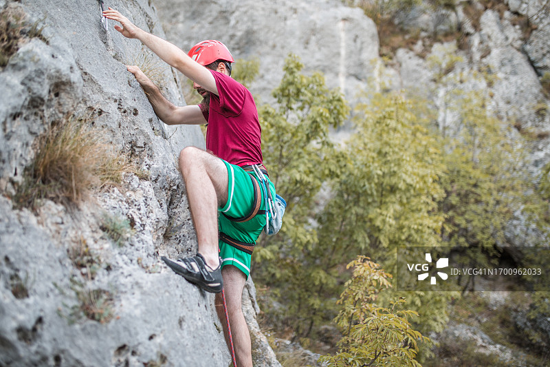 一名戴着防护头盔的男子攀登一座山，享受他最喜欢的极限运动——登山图片素材