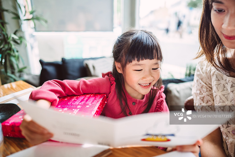 可爱小女孩在餐厅里阅读生日贺卡，收到妈妈的生日礼物图片素材