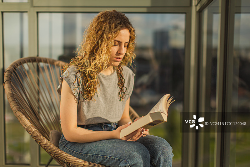 卷发红发女子在阳台椅子上看书图片素材