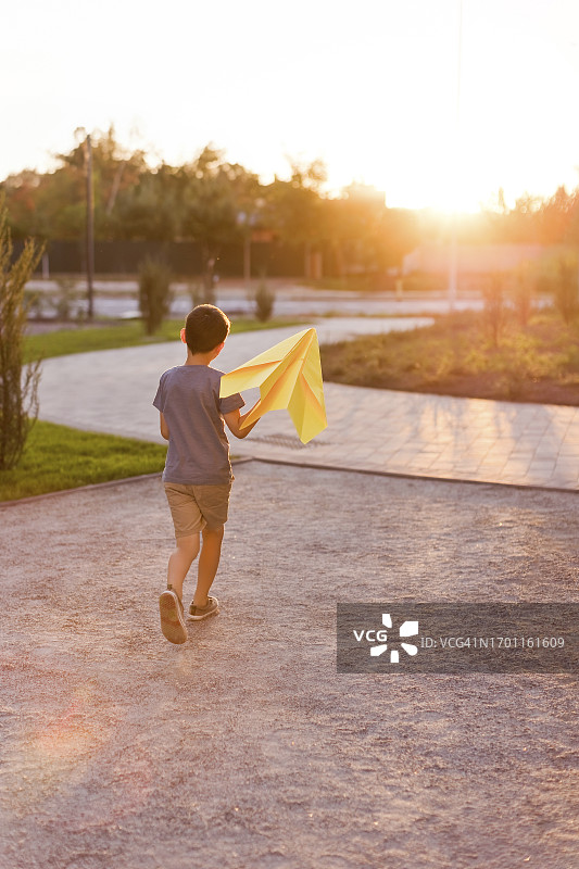 男孩拿着纸飞机在公园的沙地上行走图片素材