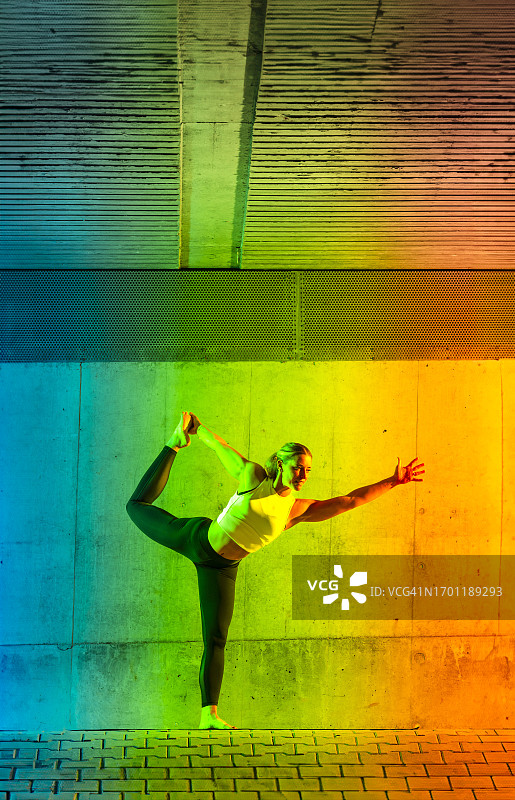 在霓虹色墙前做弓式瑜伽的女人图片素材
