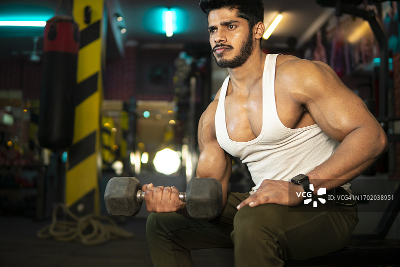 在健身房用哑铃锻炼的健壮年轻人图片素材