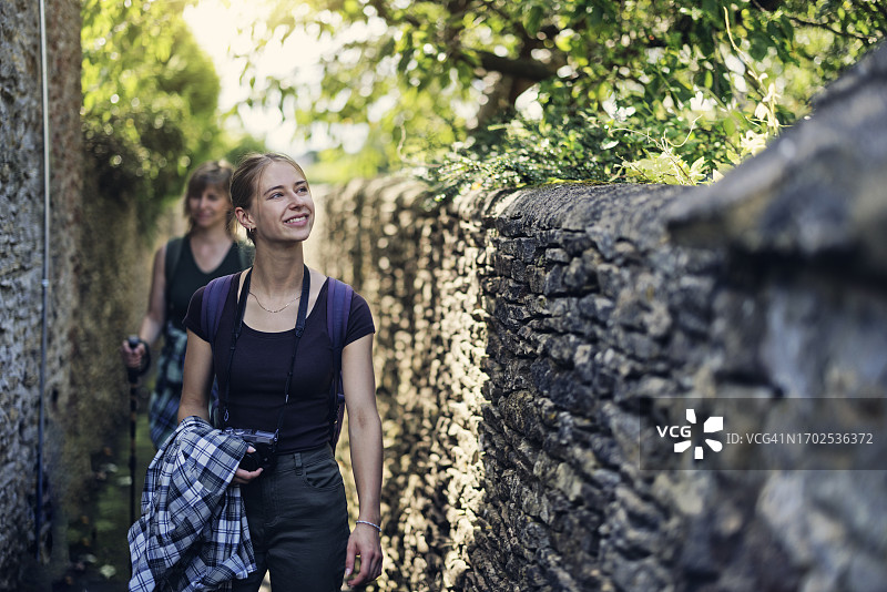 科茨沃尔德：母亲和十几岁的女儿在小屋间的小路上散步图片素材