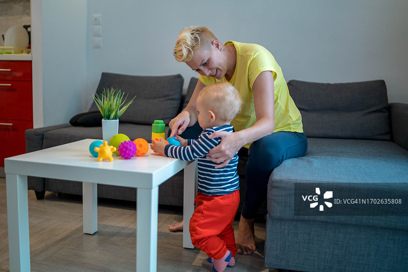 年轻的母亲和她的男宝宝在起居室里玩耍图片素材
