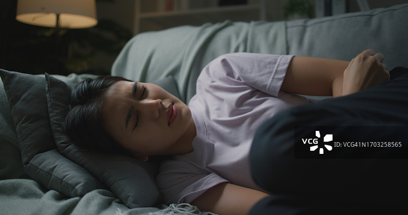 躺在沙发上不快乐的生病亚洲年轻妇女图片素材