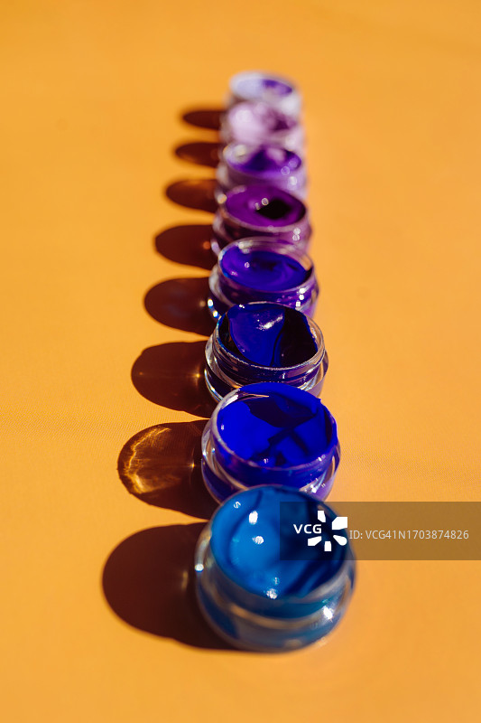 橙色背景上成排的蓝色和紫色丙烯颜料管图片素材