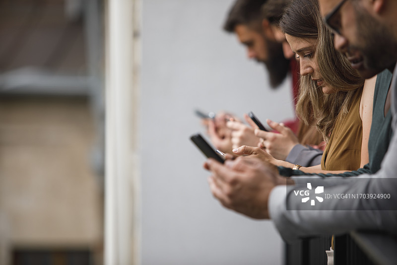 倚靠在阳台栏杆上使用智能手机的商务人士图片素材