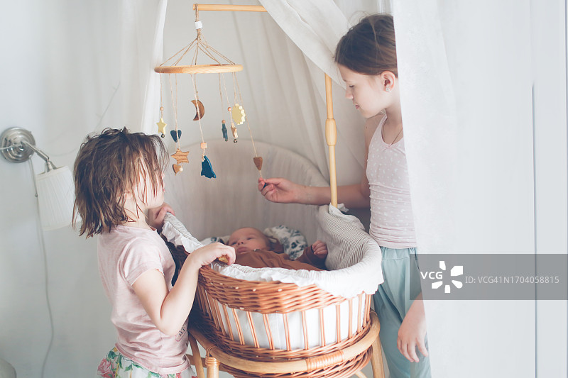 姐妹情深：姐妹俩在柳条摇篮旁看着弟弟的温馨时刻图片素材