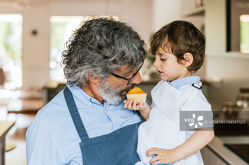爷爷和男孩穿着围裙吃自制松饼图片素材