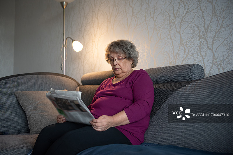 老年妇女在家里的沙发上看报纸图片素材