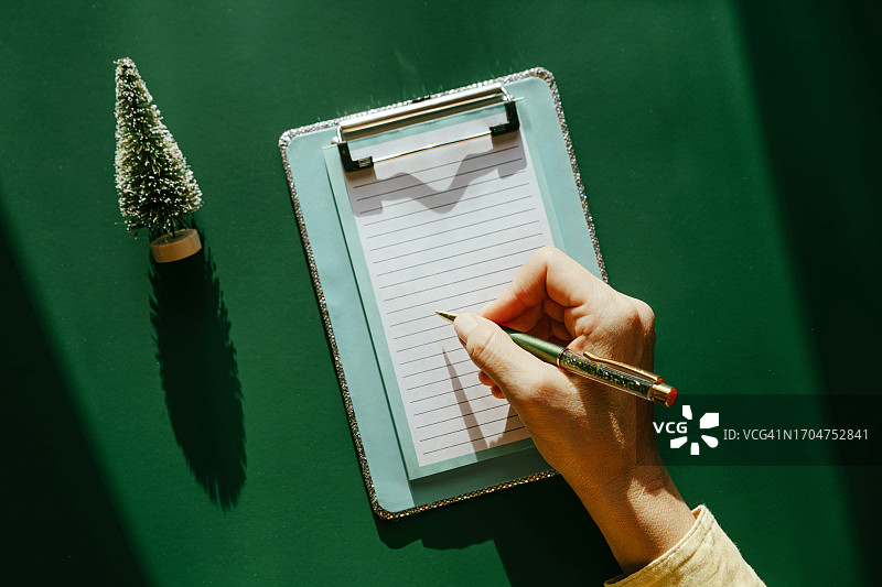 绿色背景上手持纸和笔的蓝色笔记本图片素材