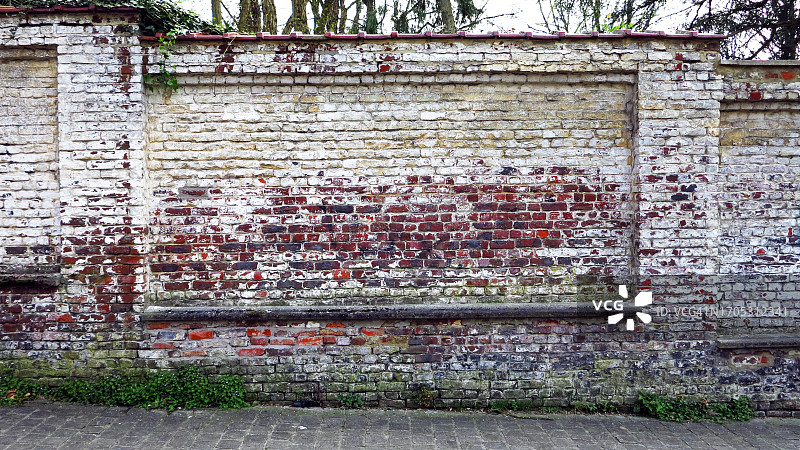 布鲁塞尔的旧砖墙上风化的白色油漆，杂草和鹅卵石街道图片素材