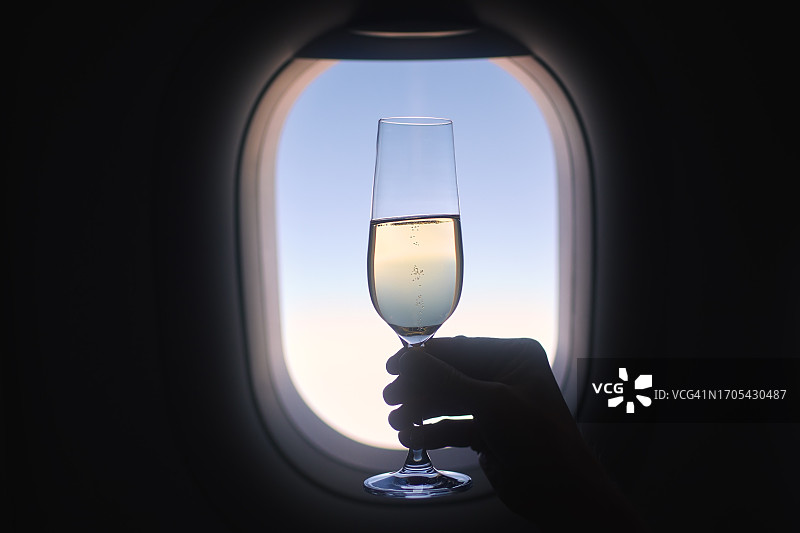 手持香槟酒杯，背景为飞机舷窗图片素材