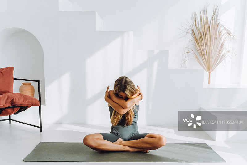 清晨，在白色房间里做瑜伽呼吸练习时，抱着自己并遮住脸的金发女人图片素材