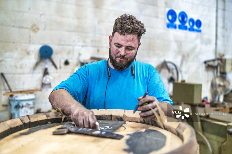 在雪利酒桶厂工作的工人测量酒桶直径，医生用粉笔在桶上标记图片素材