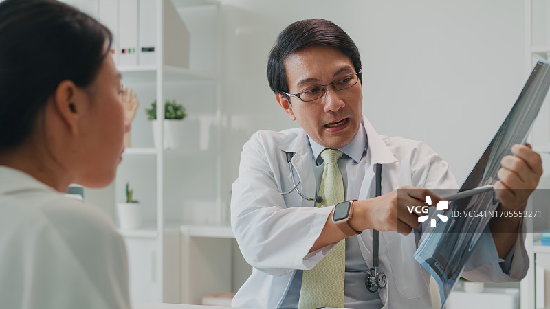 亚洲男医生向女患者展示肺部X光检查结果，讲解医疗保健图片素材