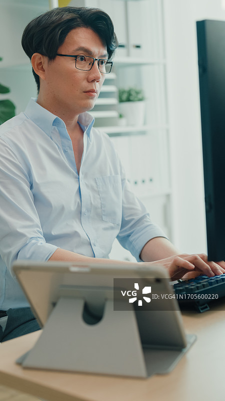 年轻的亚洲男人软件开发人员使用电脑编写代码，坐在办公桌前，多个屏幕在办公室工作。程序员开发。竖屏图片素材