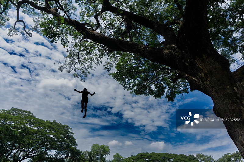 蓝色多云天空下从树上跳跃的人仰视角度图片素材