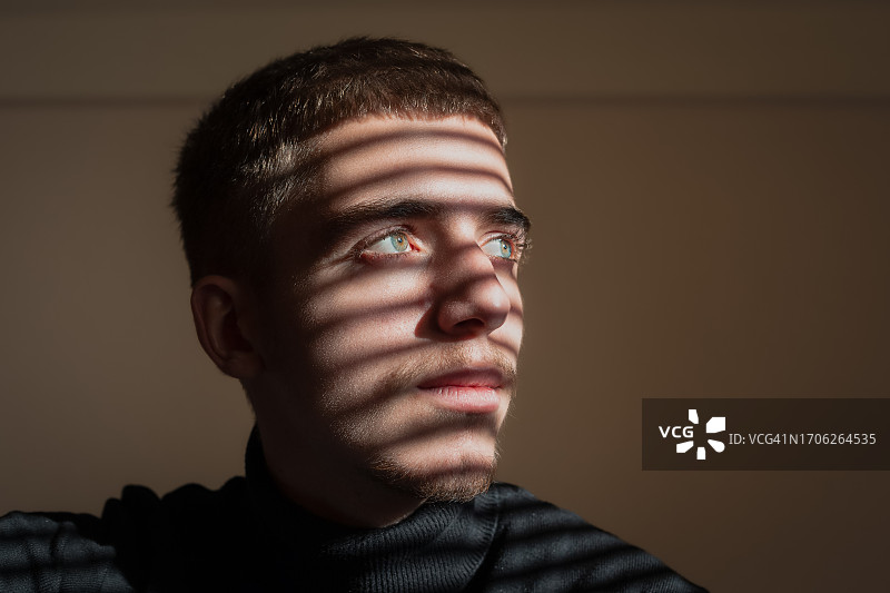 坐在百叶窗阴影中沉思的男子特写，心理健康问题概念图片素材