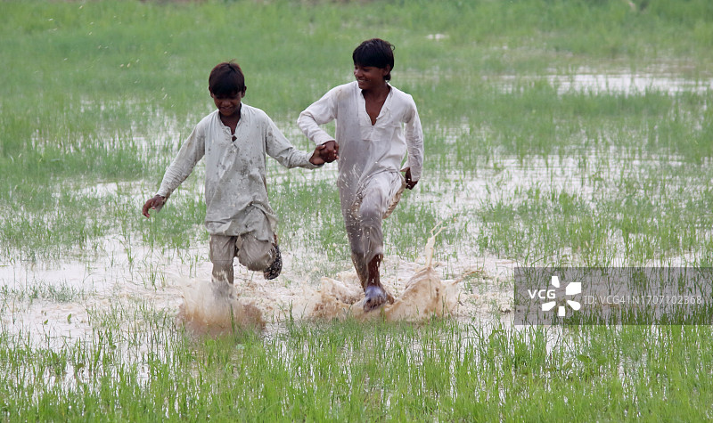 两个男孩在满是雨水的草地上奔跑，水花四溅图片素材