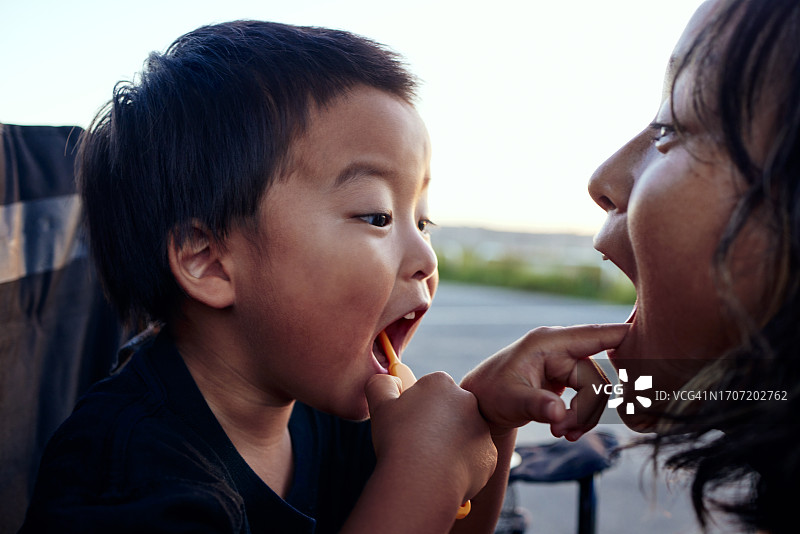母亲在露营的早晨与刷牙的儿子互动图片素材