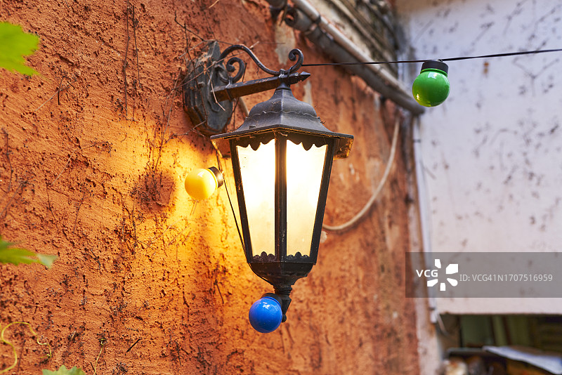 房屋外墙上带有彩色灯泡的复古风格灯或灯笼的侧面照图片素材