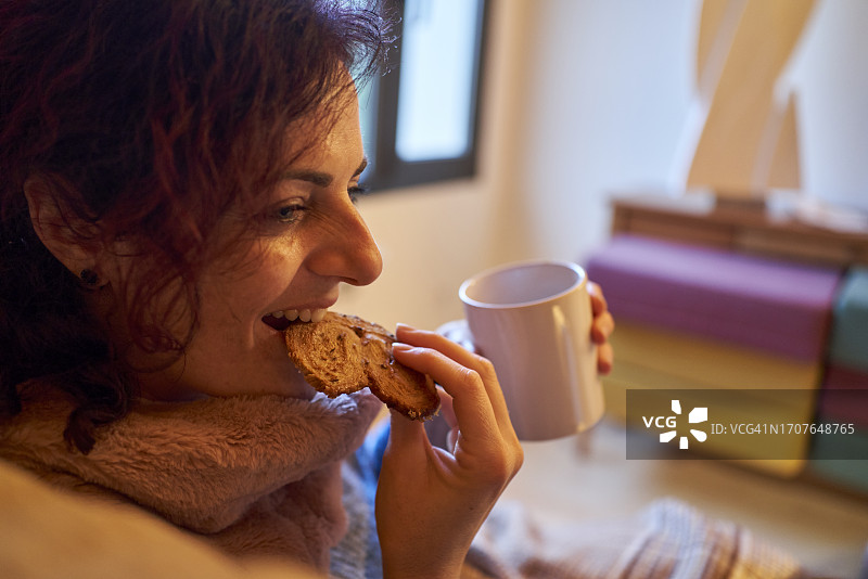 坐在沙发上喝热巧克力、吃甜饼干的女子侧身像图片素材