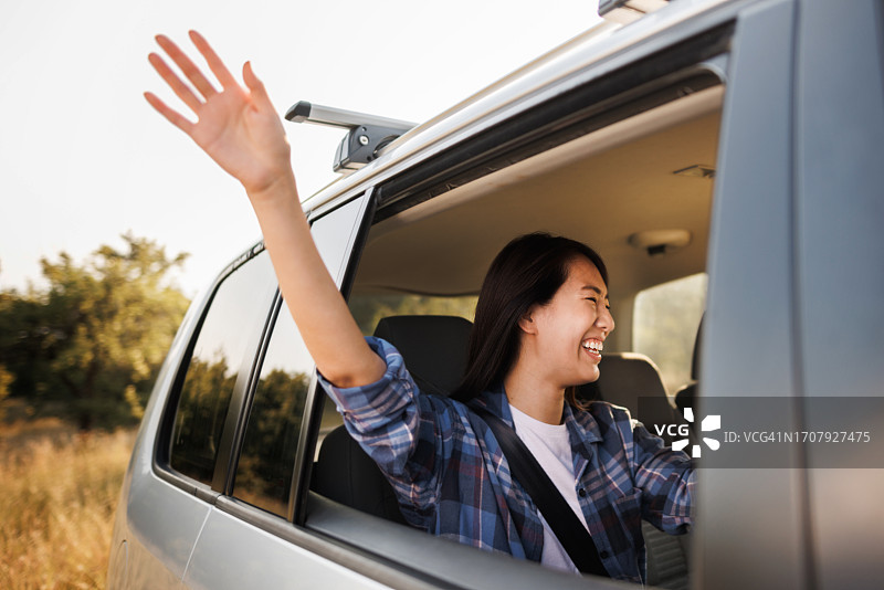 快乐的年轻亚洲女性坐在车里笑着，手伸出窗外图片素材