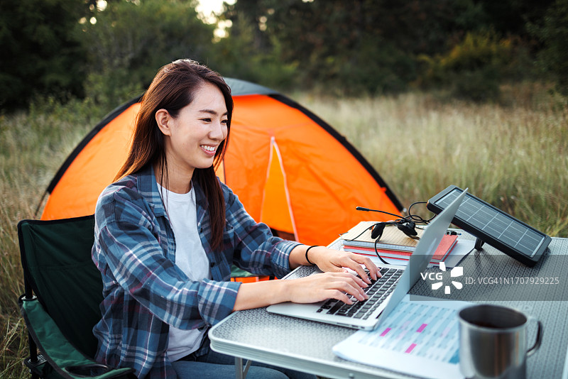 在露营帐篷附近使用笔记本电脑工作的年轻漂亮微笑女人图片素材