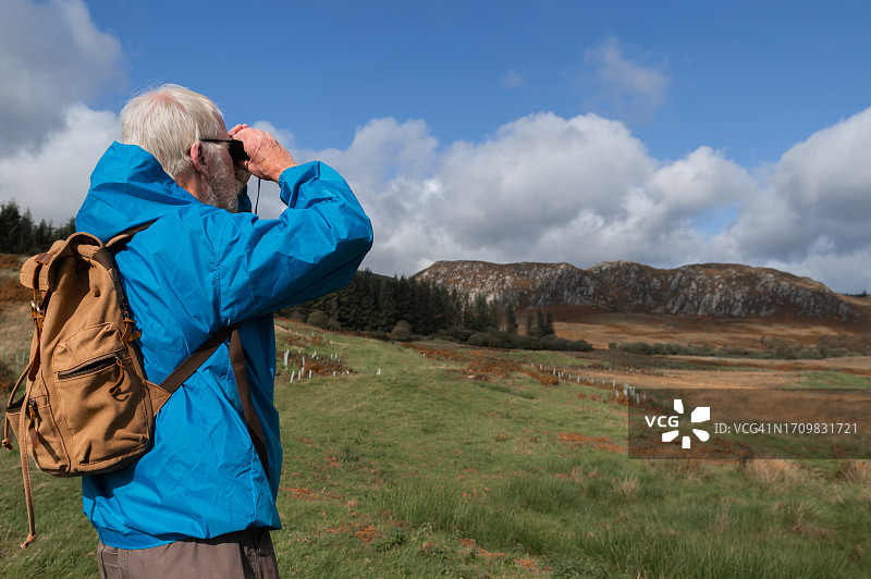 在乡村使用双筒望远镜的老年男人图片素材