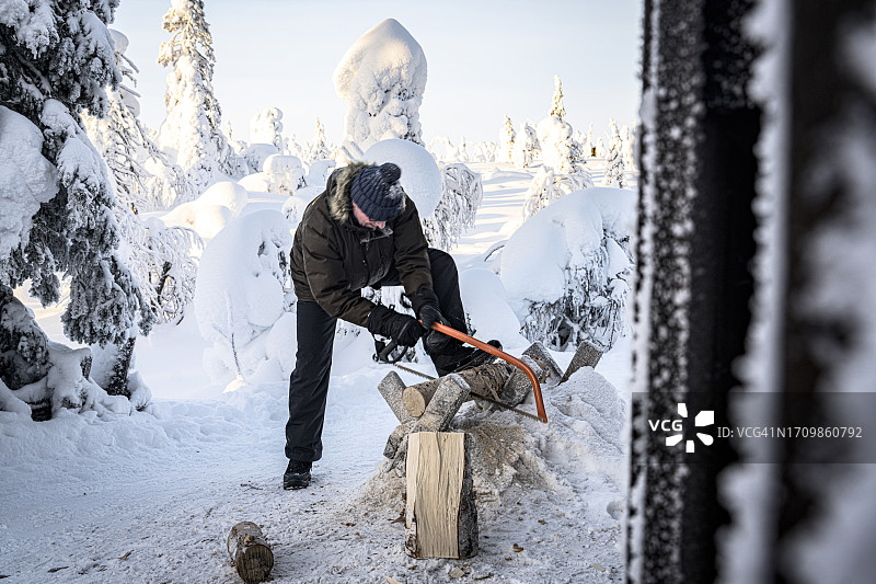 男人在冰雪覆盖的森林里锯木柴图片素材