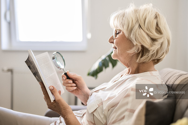 老年妇女在家使用放大镜阅读书籍图片素材