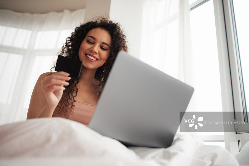 黑皮肤女孩使用笔记本电脑进行网上购物。在床上进行网上购物。用信用卡购买。在线支付。图片素材