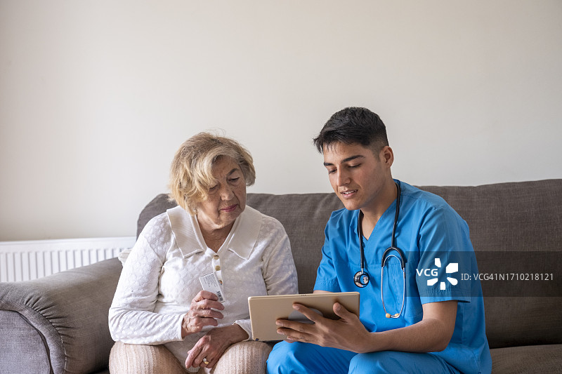 年轻男护士展示老年妇女如何使用数字平板电脑服药图片素材
