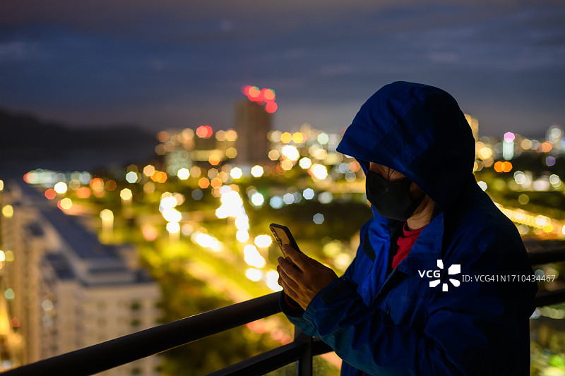 穿着帽衫的男人在黑暗中手持手机，背景是城市图片素材