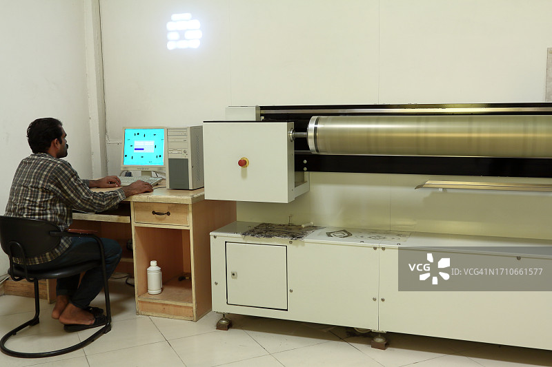 一个男人在纺织滚筒丝网雕刻部门用电脑工作图片素材