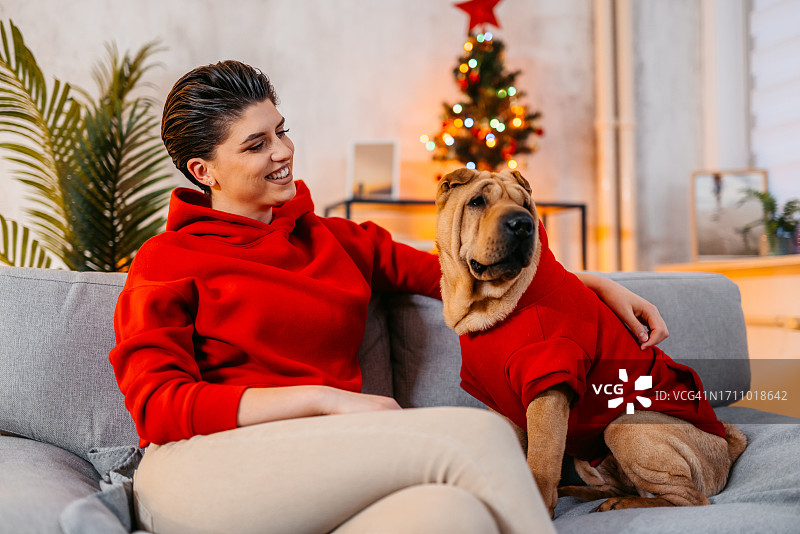 年轻女人在圣诞节与她的狗坐在沙发上图片素材
