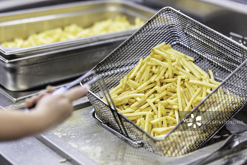 女人在商业厨房手拿装有炸薯条的煎锅图片素材