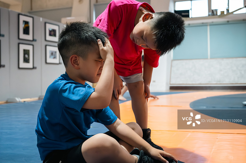 在摔跤训练中，一个年轻男孩头部受伤，他的队友给予关心和照顾图片素材