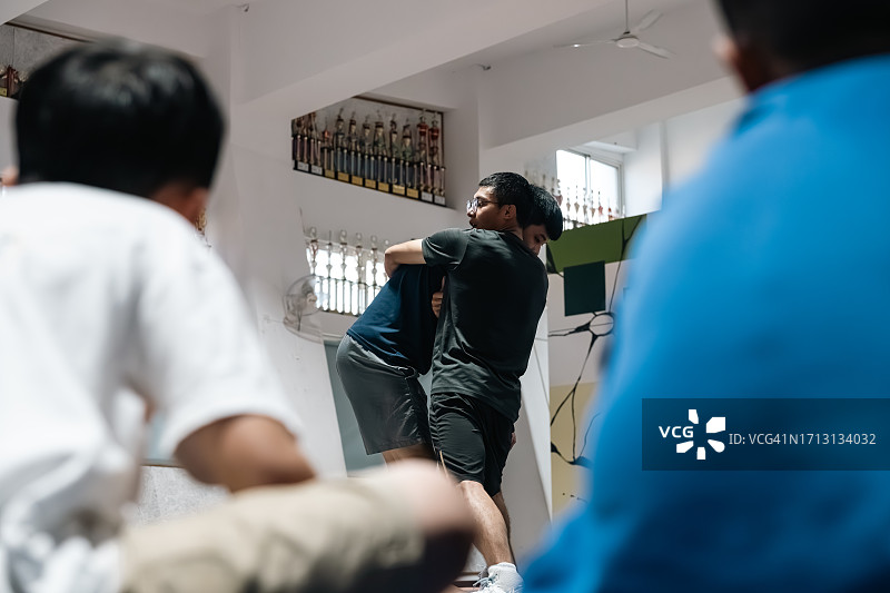 一群学龄儿童坐在场边，认真听体育教练的示范讲解图片素材