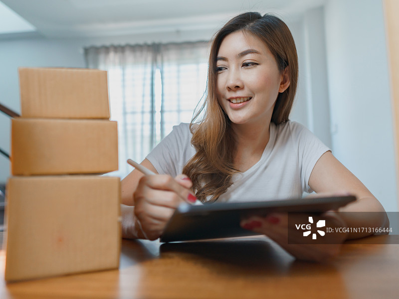 女人使用平板或智能手机，检查订单，周围是包裹箱。电商企业主处理在线订单和发货图片素材