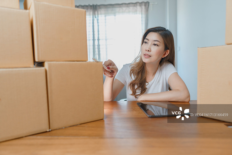 女商人检查订单，周围是包裹箱。拥有纸板箱的在线订单和配送业务的女老板。图片素材