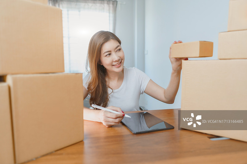 女商人检查订单，周围是包裹箱。拥有纸板箱的在线订单和配送业务的女老板。图片素材