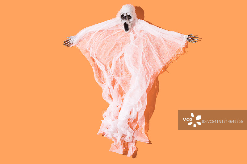 橙色背景上有着骨骼手和虚幻身体的阴森生物：万圣节、鬼魂概念图片素材